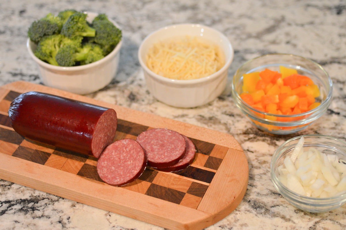 Sliced summer sausage on a cutting board with vegetables and dip