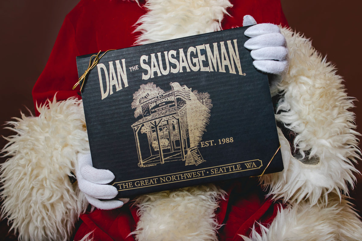 Santa holding a black and gold Dan the Sausageman gift box