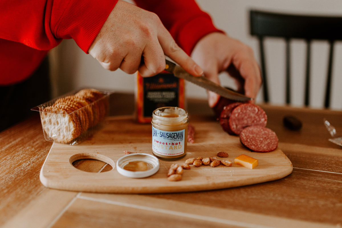 Slicing summer sausage on a wooden board with mustard and crackers