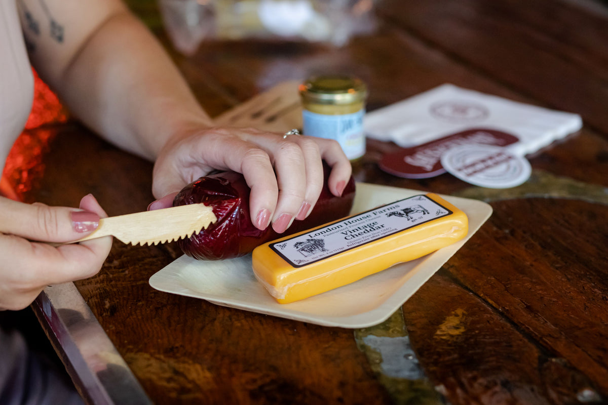 Cutting cheese next to a summer sausage on a wooden board